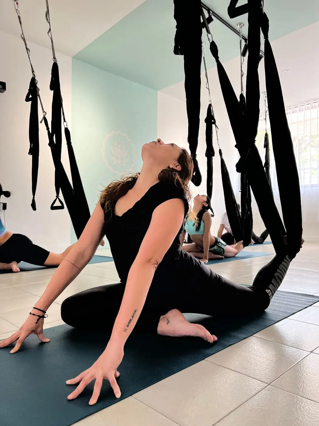 Alumna estirando en el tapete, con una pierna en el columpio, durante una clase